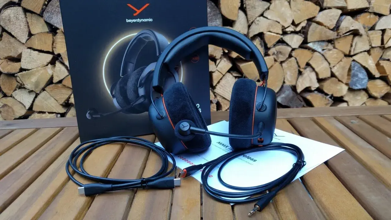 Beyerdynamic MMX 150 Test: Gaming-Headset mit Mikrofon, Kabeln und Anleitung auf Holztisch vor Holzstapel.