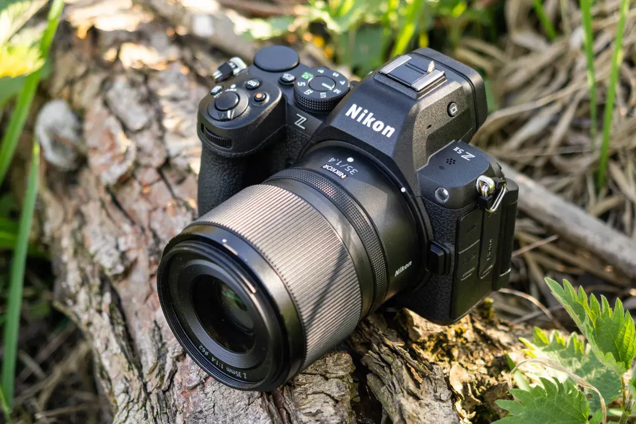 Aparat Nikon Z5 II z obiektywem Nikkor 35mm f/1.4 leży na spróchniałym drewnie, otoczony zielenią.