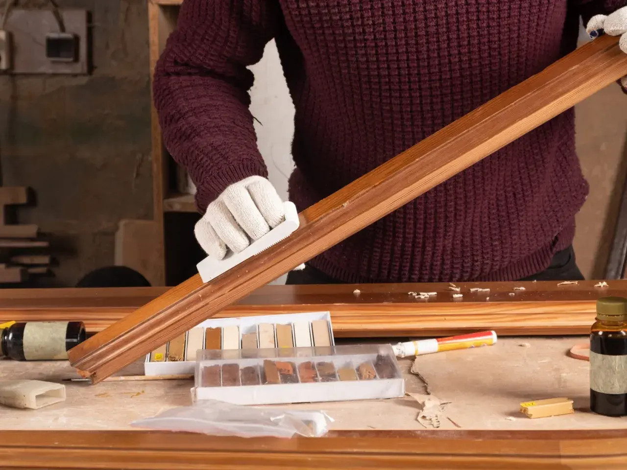 Persona con guantes blancos restaura un mueble de madera, usando un bloque para lijar y kits de retoque.
