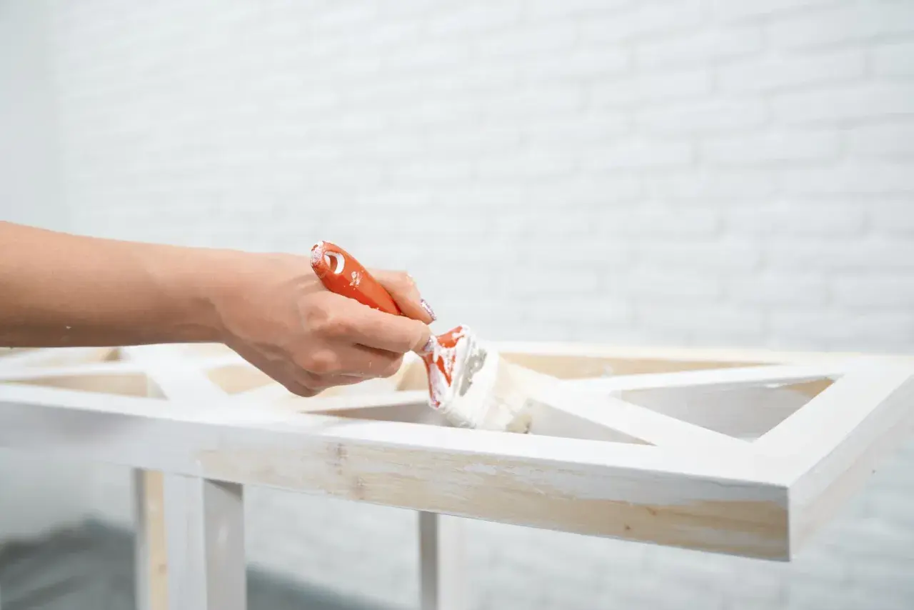 Mano che dipinge un mobile in legno con vernice a gesso, per un effetto shabby chic.