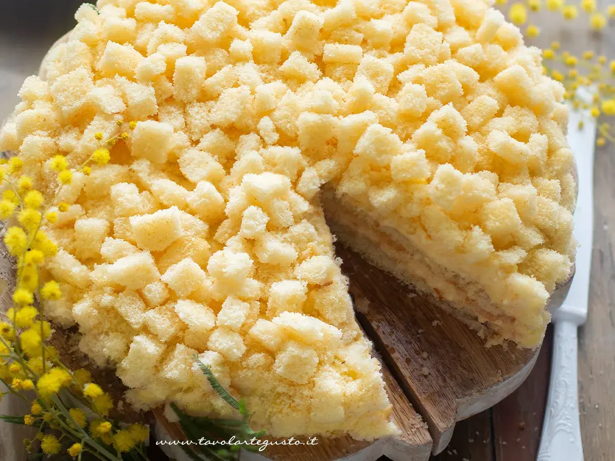 Una deliziosa torta mimosa, ricoperta di soffici briciole di pan di Spagna, con un rametto di mimosa a decorare.
