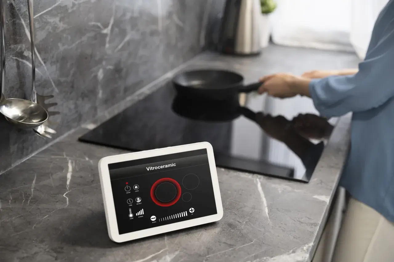 Cocina moderna con vitrocerámica y tablet para controlar electrodomésticos inteligentes. Una persona cocina en la placa de inducción.