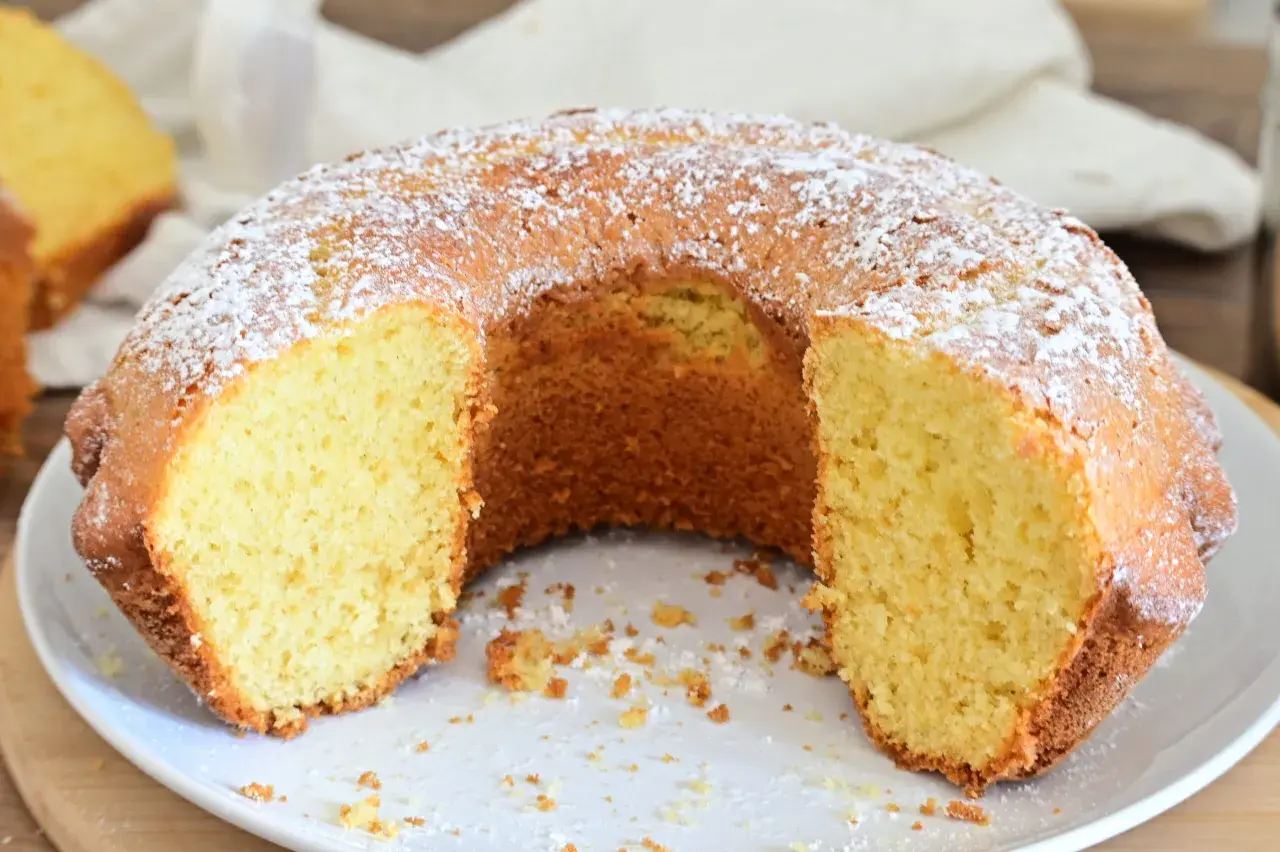 Una ciambella soffice, cosparsa di zucchero a velo, attende di essere gustata. La sua consistenza invitante promette un momento di puro piacere.