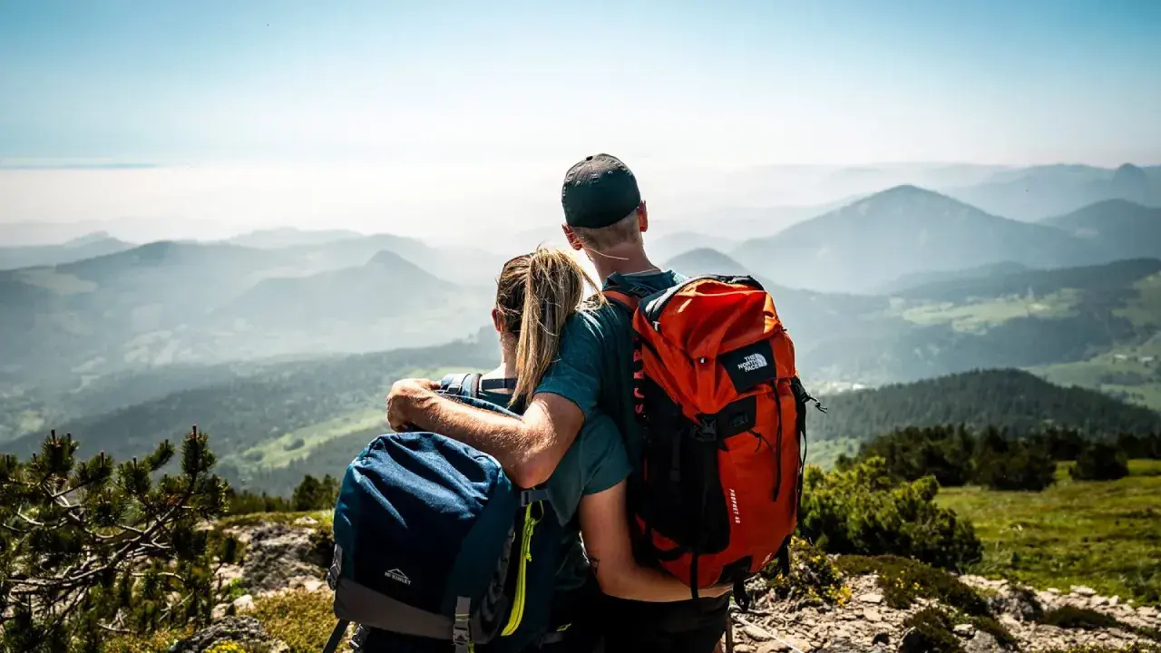 Couple en randonnée, admirant le panorama des montagnes de la Grande Ardèche. Sacs à dos orange et bleus, vue imprenable.