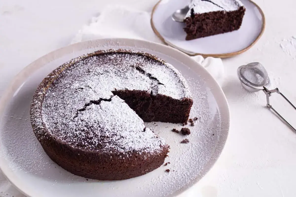 Gâteau au chocolat saupoudré de sucre glace, une part coupée. Idéal pour savoir par quoi remplacer le beurre dans un gâteau au chocolat.