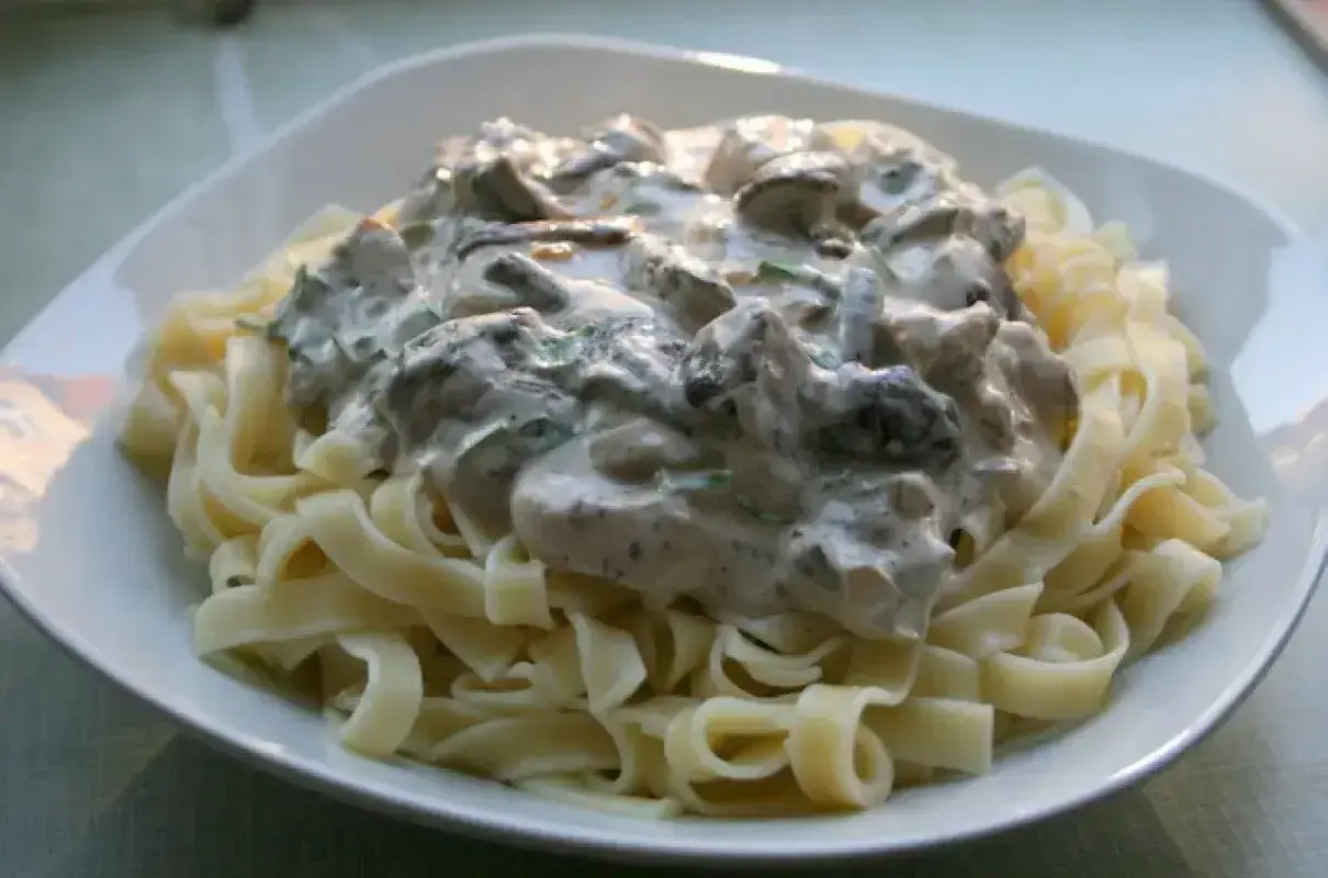 Pyszne tagliatelle z grzybami w kremowym sosie, podane na białym talerzu. Idealne danie dla miłośników grzybów.