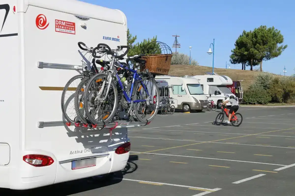 Camping-car avec vélos à l'arrière. Un cycliste s'entraîne sur un parking. Avis sur aire de camping-car.