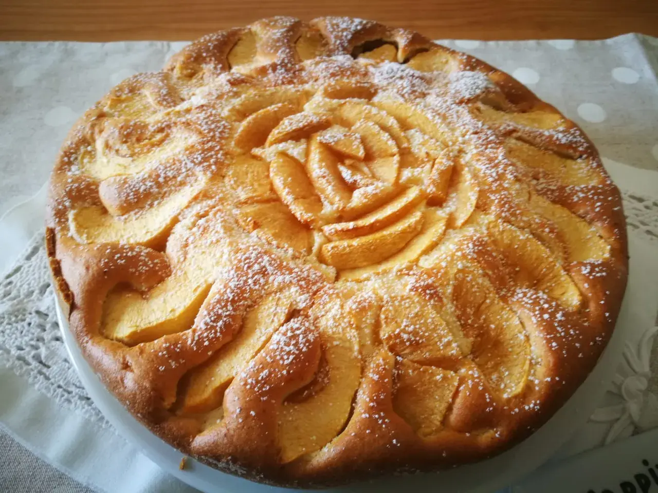 Una deliziosa torta di mele senza glutine, decorata con fettine di mela a forma di rosa e spolverata di zucchero a velo.