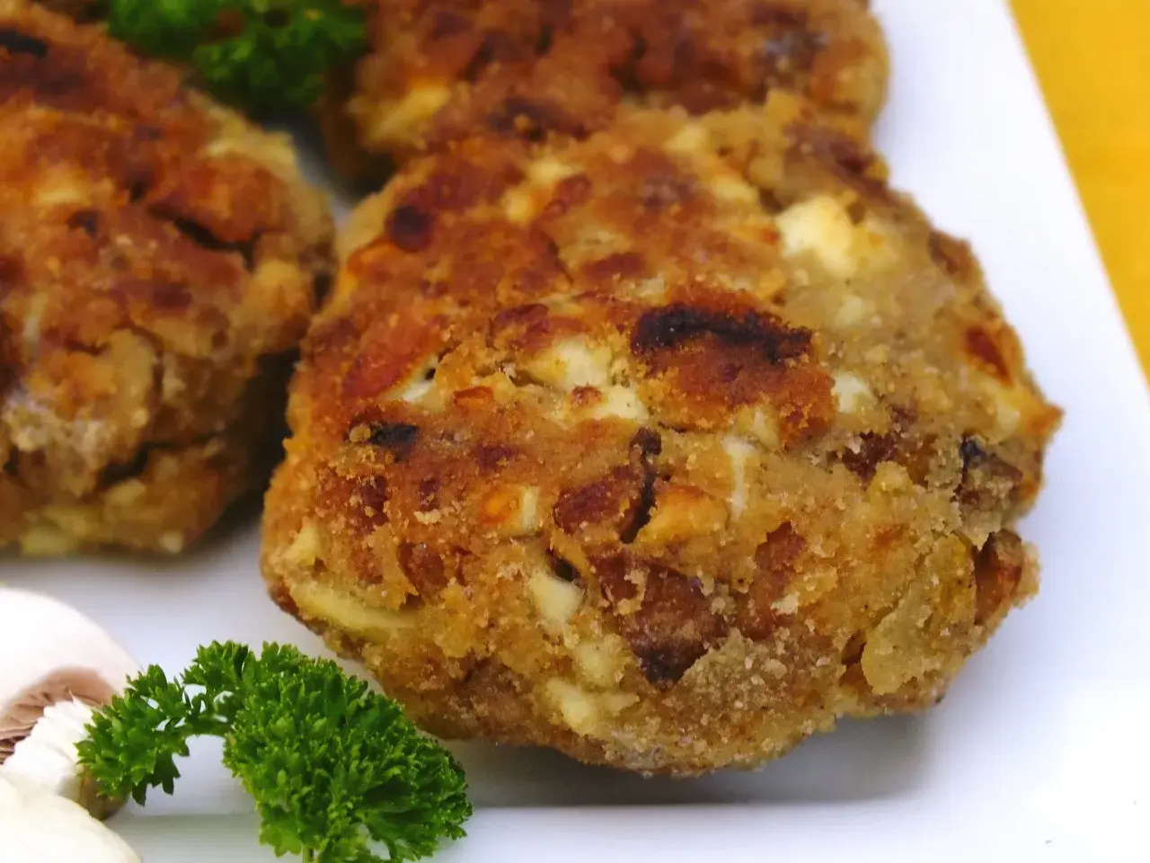 Złociste kotlety z pieczarek, chrupiące i aromatyczne, podane z natką pietruszki i plasterkami pieczarki.