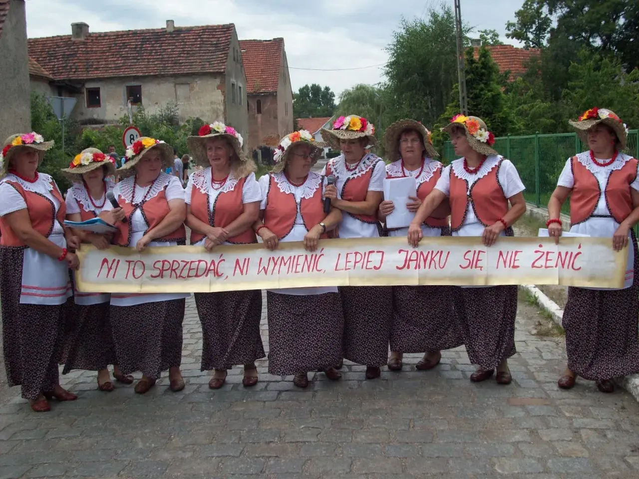 Kobiety w ludowych strojach trzymają transparent z napisem "Ni to sprzedać, ni wymienić, lepiej Janku się nie żenić" - śmieszne teksty na bramy weselne.