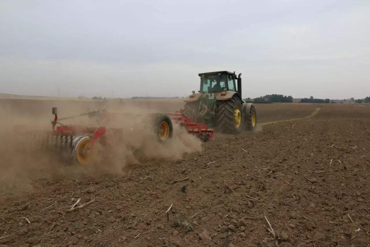 Traktor z agregatem uprawowym wykonuje uprawę bezorkową, wzbijając tumany kurzu na polu.