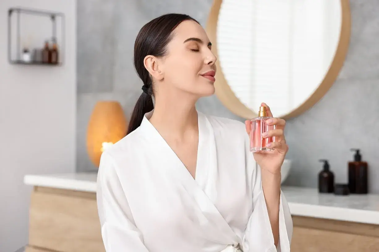 Kobieta w szlafroku rozpyla perfumy. Mgiełka od perfum różni się intensywnością zapachu i trwałością.