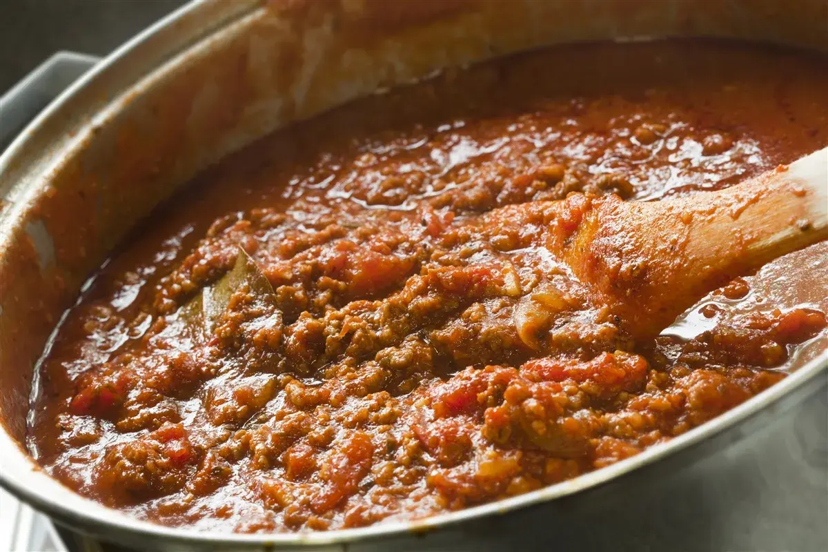 Salsa boloñesa burbujeante en una olla, con una cuchara de madera removiendo la carne picada y los tomates.