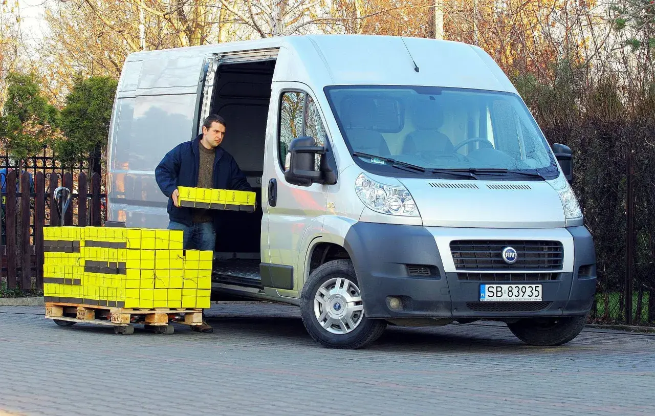Mężczyzna rozładowuje żółte paczki z Fiata Ducato 2.3.