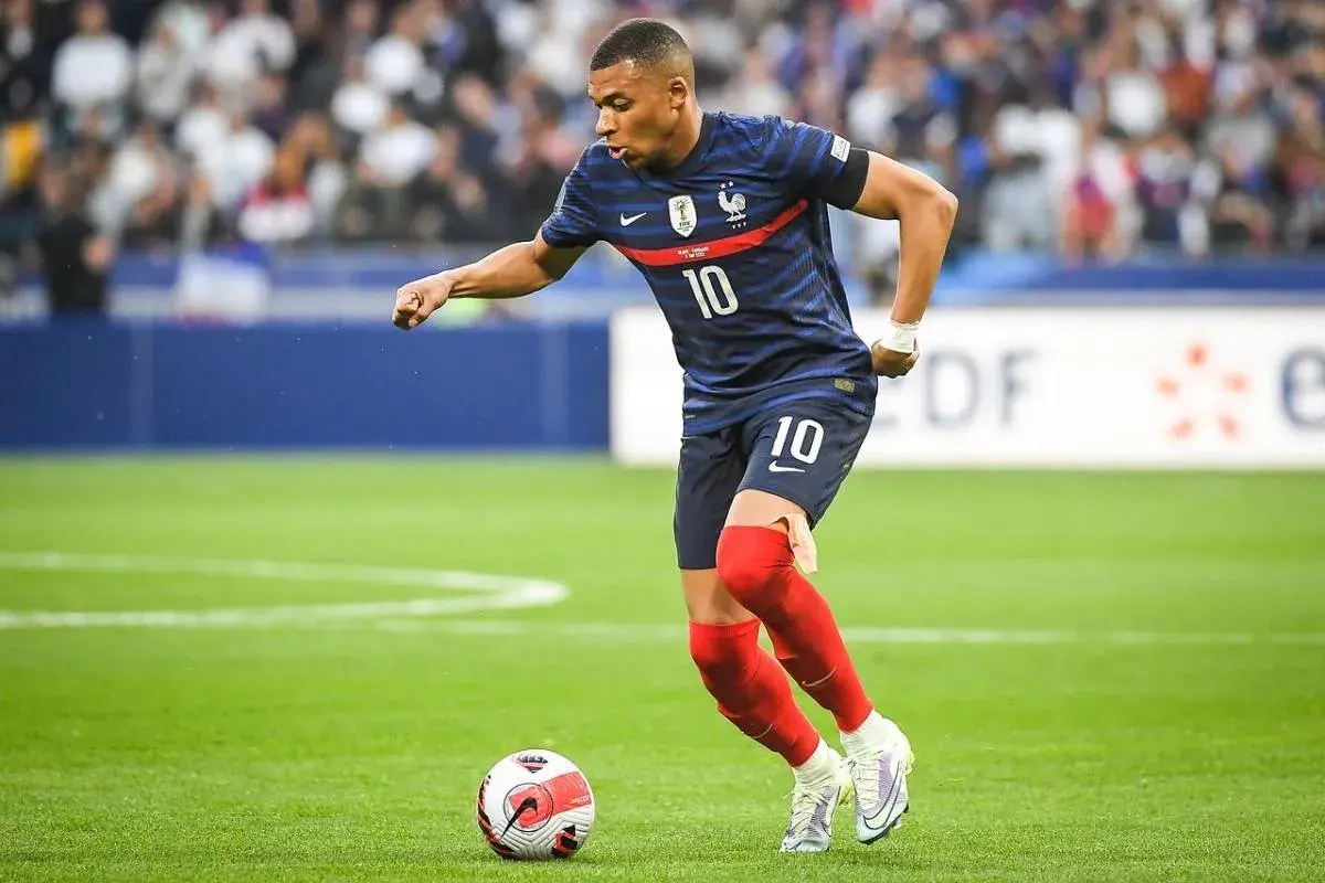 Kylian Mbappé w niebieskiej koszulce z numerem 10, w czerwonych getrach, wykonuje najszybszy sprint w piłce nożnej, prowadząc piłkę.
