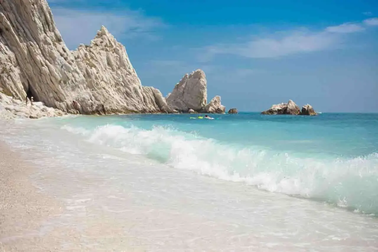 Spiaggia delle Due Sorelle: onde turchesi lambiscono la riva, rocce bianche imponenti si ergono sul mare azzurro, un paradiso incontaminato.