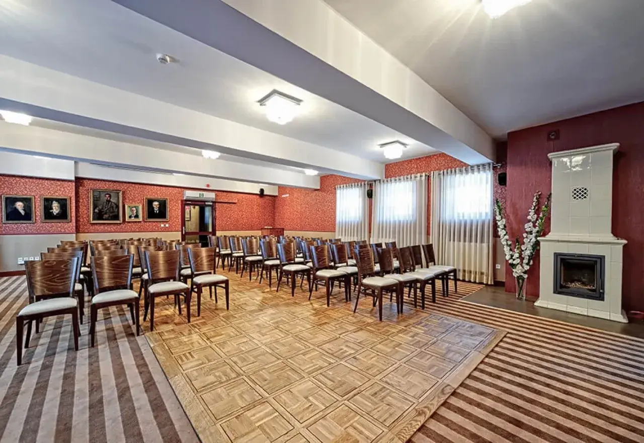 Elegancka sala konferencyjna w Lanckorona Hotel Modrzewiówka, z rzędami krzeseł, portretami na ścianach i ozdobnym piecem.