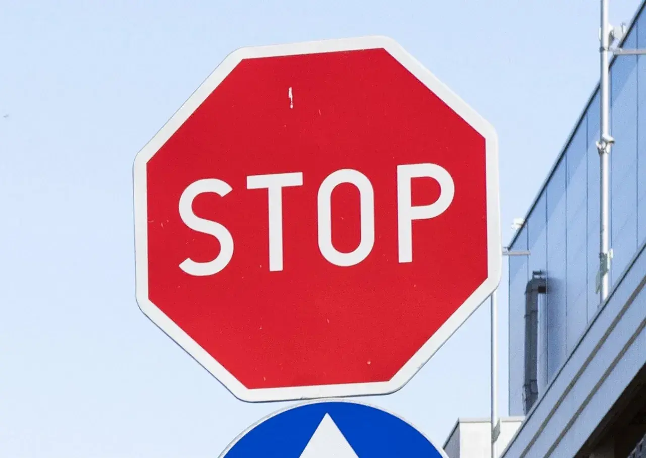 Czerwony znak stop z białym napisem. Obok nowoczesny budynek.