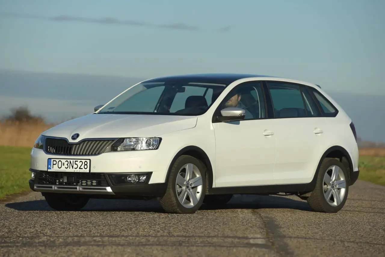 Biała Skoda Rapid z czarnym dachem, z widocznymi światłami i żarówkami, zaparkowana na drodze.