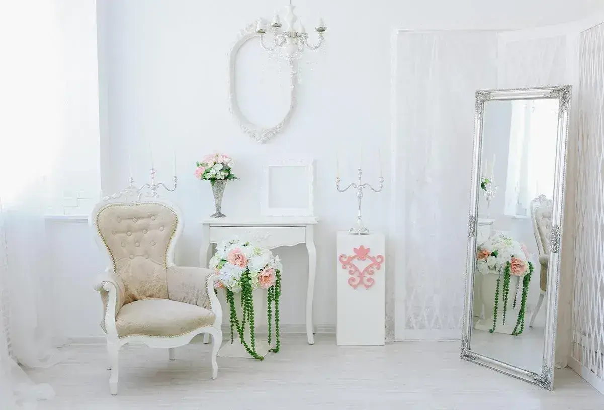 Jasny salon w stylu shabby chic z fotelem, lustrem i bukietami kwiatów.