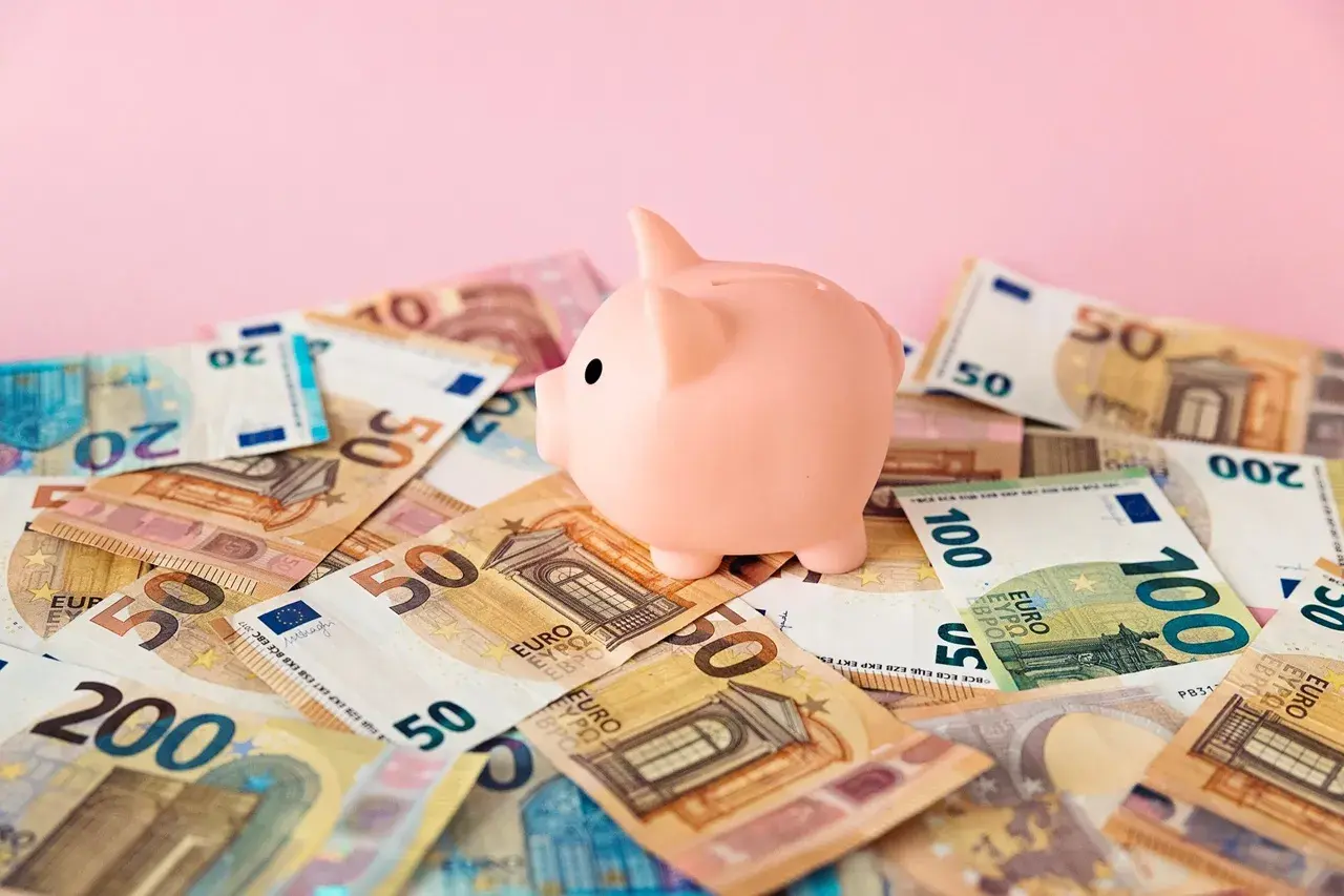 Różowa świnka-skarbonka na stosie banknotów euro. Zastanawiasz się nad oprocentowaniem konta walutowego?