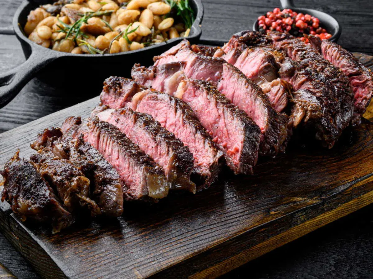 Côte de bœuf juteuse, tranchée et prête à être dégustée. Parfaitement cuite sur la plancha, accompagnée de haricots et de poivre rose.