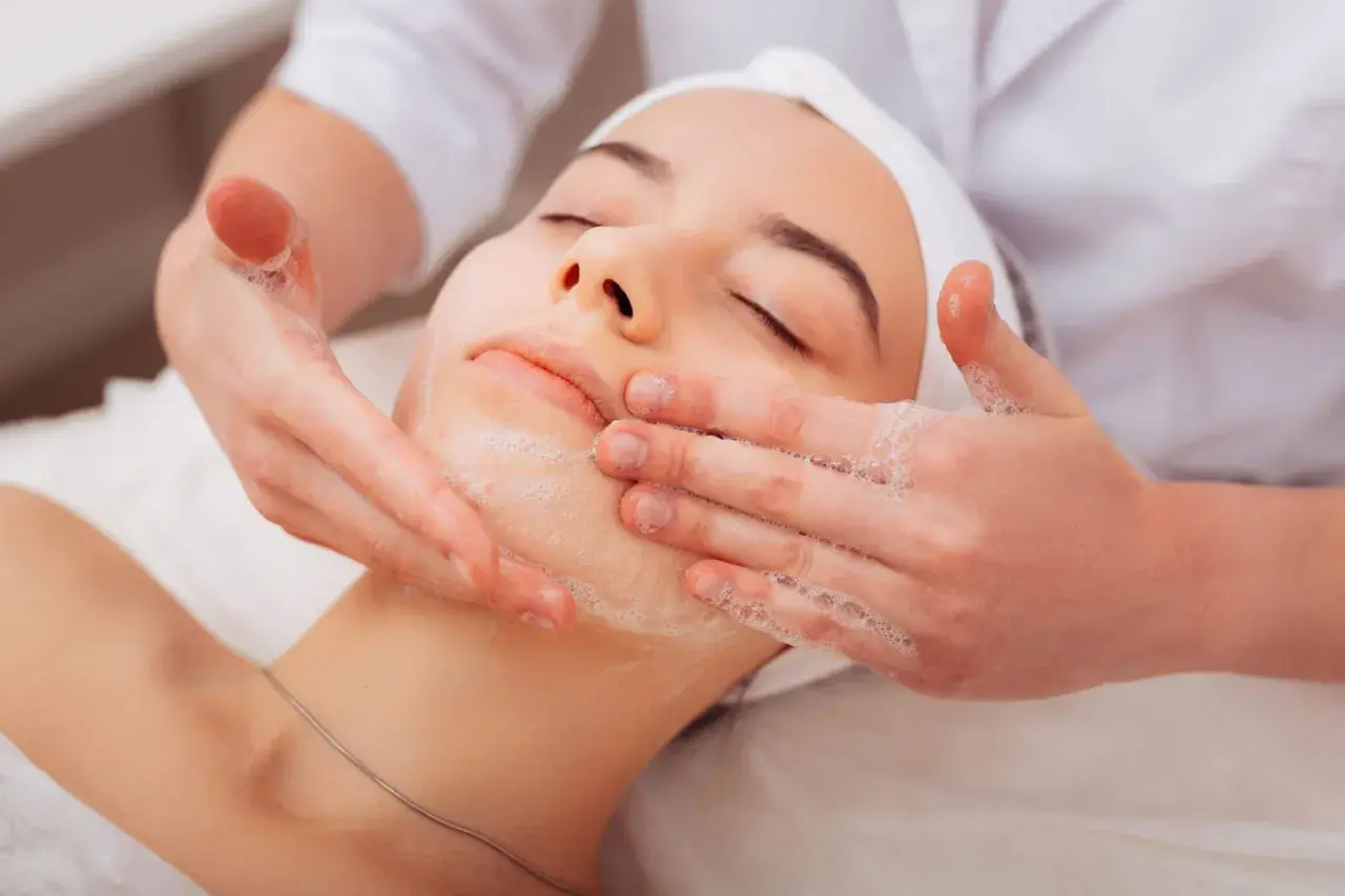 Una donna riceve un trattamento viso con schiuma. Per una pelle luminosa, chiediti ogni quanto fare la pulizia del viso.
