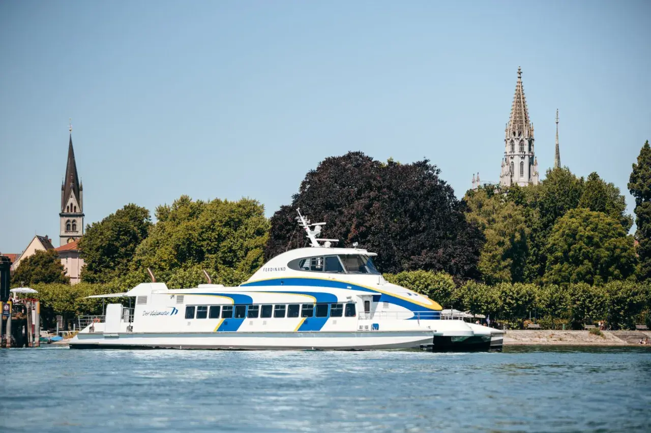 Schnelles Katamaran-Schiff auf dem Bodensee, mit Kirchtürmen von Friedrichshafen und Konstanz im Hintergrund.