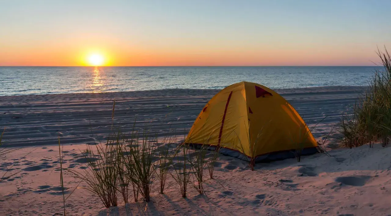 Żółty namiot na piaszczystej plaży, z widokiem na spokojne morze i zachodzące słońce. Idealne miejsce na nocleg, gdzie pole namiotowe nad morzem wita o poranku.