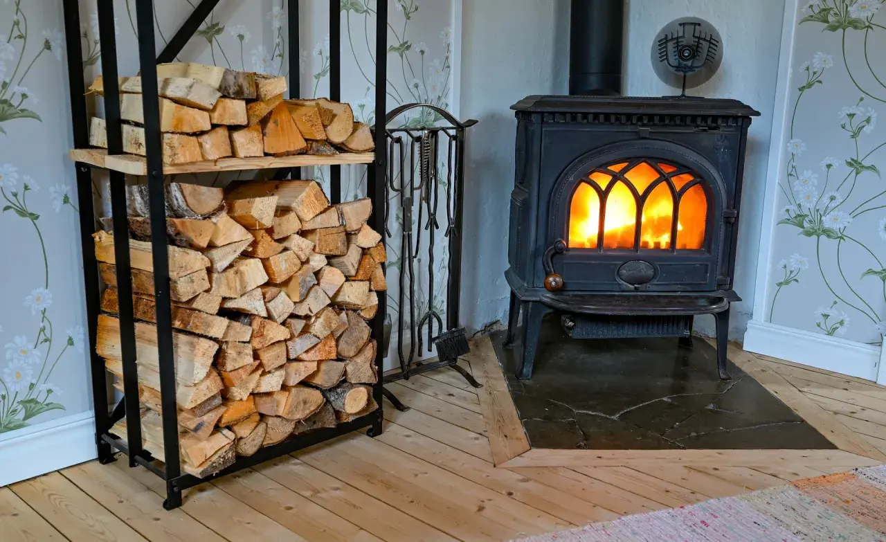 En mysig brasa sprakar i en gjutjärnskamin. Bredvid står en hylla fylld med ved, redo att installera braskamin för värme och trivsel.