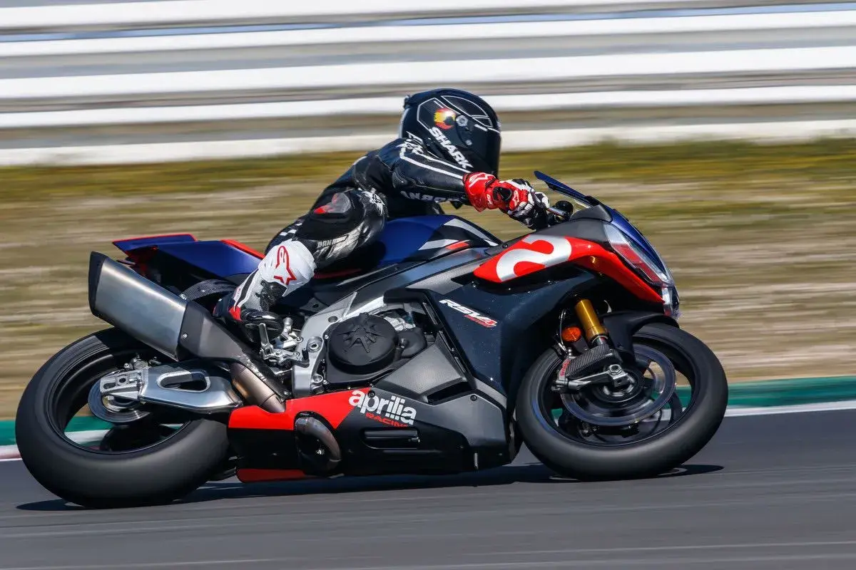 Piloto en una Aprilia RSV4 1100 en circuito, con traje de cuero negro y rojo, casco Shark.