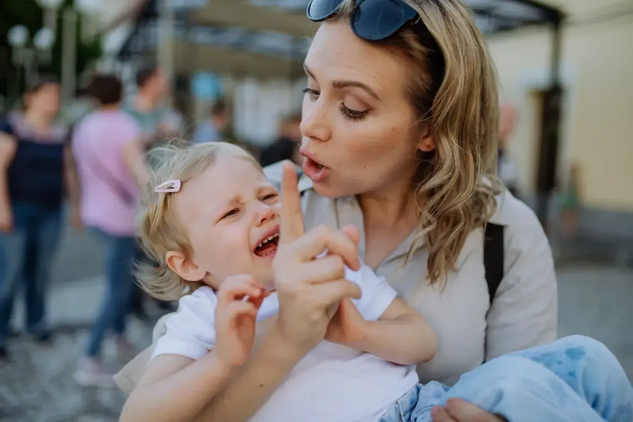 Bambina piange mentre la madre, forse afflitta da depressione, cerca di calmarla. Gli effetti della madre depressa sui figli adulti sono complessi.