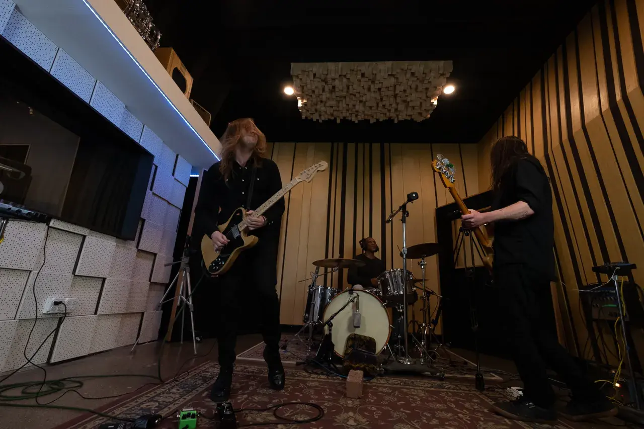 Zakk Cervini and his band rock out in a studio, with a guitarist in the foreground, a bassist to the right, and a drummer in the background.