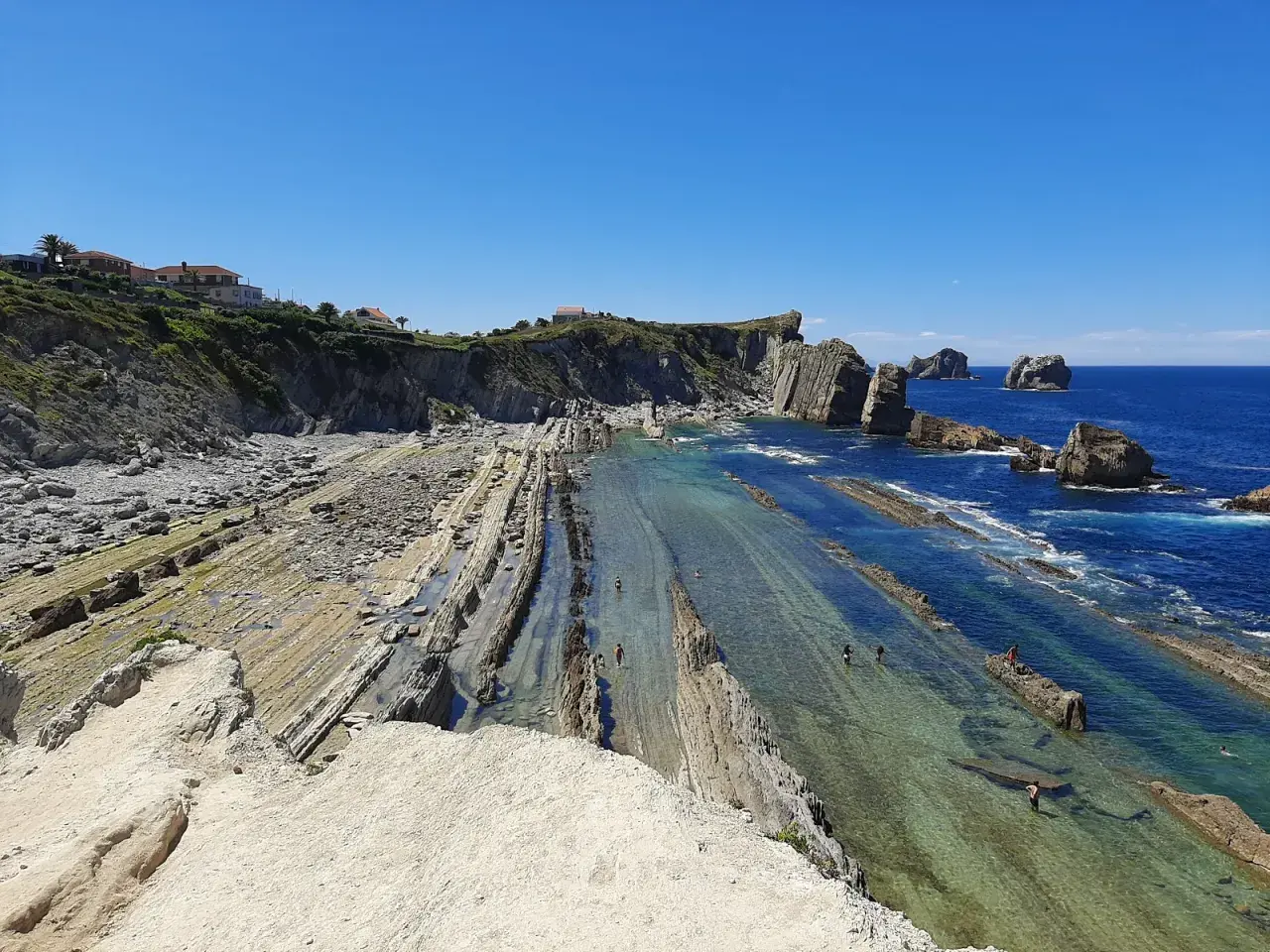Espectacular vista de la playa de Arnia con sus formaciones rocosas y aguas cristalinas. Personas disfrutan del mar.