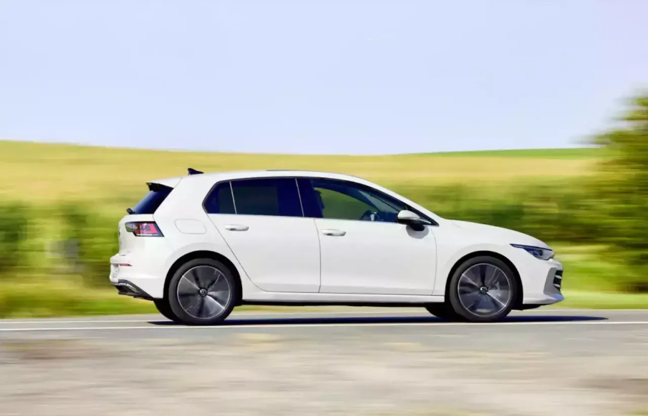 Biały hatchback pędzi po drodze, otoczony rozmytymi zielonymi polami i błękitnym niebem.