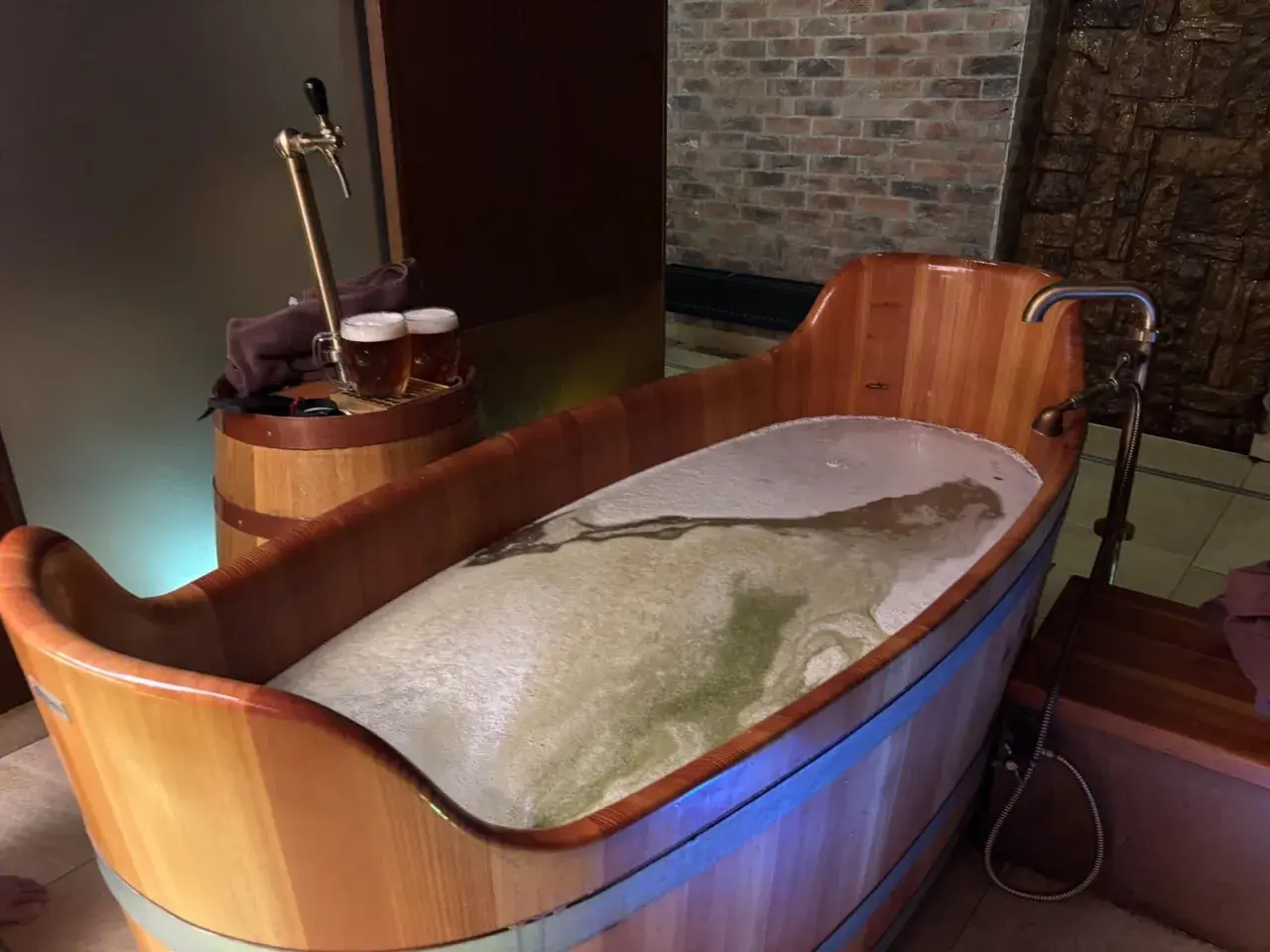 Entspannendes Bier-Wellness-Erlebnis in Tschechien: Ein hölzerner Bottich gefüllt mit schäumendem Bier, daneben ein Zapfhahn und zwei Biergläser.
