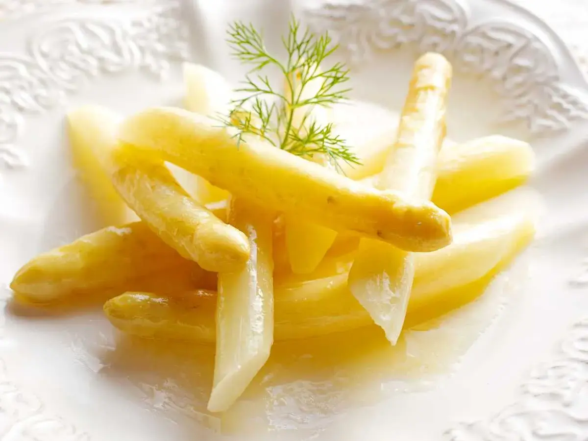Espárragos blancos tiernos, cocidos y servidos en un plato blanco con una ramita de eneldo. Una guía visual para como cocer esparragos blancos.