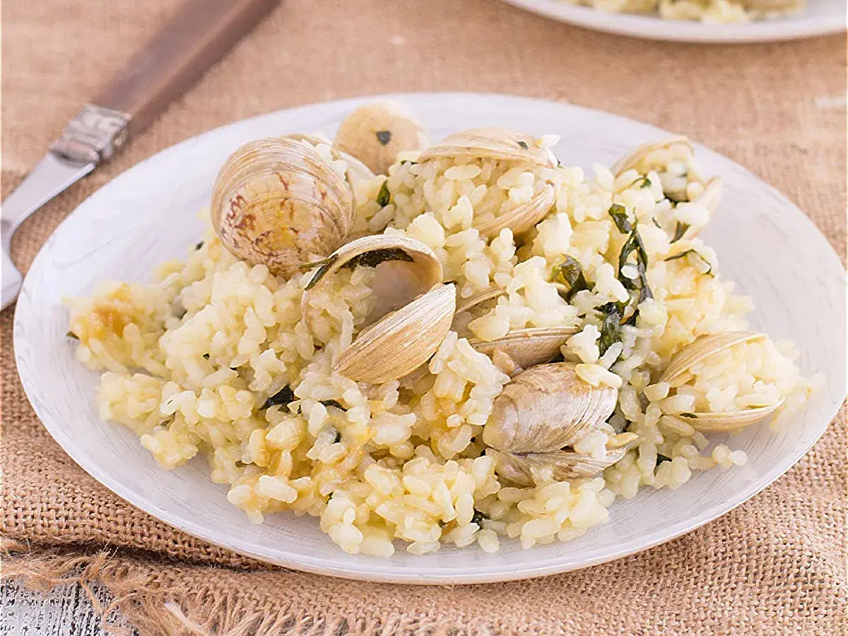 Un plato de arroz cremoso con almejas frescas, adornado con hierbas verdes. Un delicioso arroz con almejas listo para disfrutar.