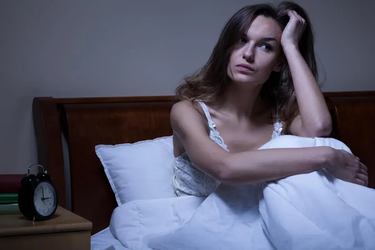 Mujer angustiada en la cama, pensando qué significa soñar que tu pareja te deja. La noche es larga y la incertidumbre la acompaña.