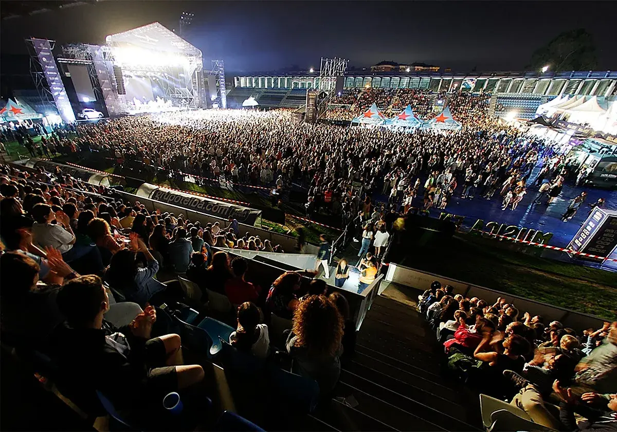 Multitud disfrutando de conciertos Torrelavega hoy. Escenario iluminado, miles de personas vibran con la música en un estadio.