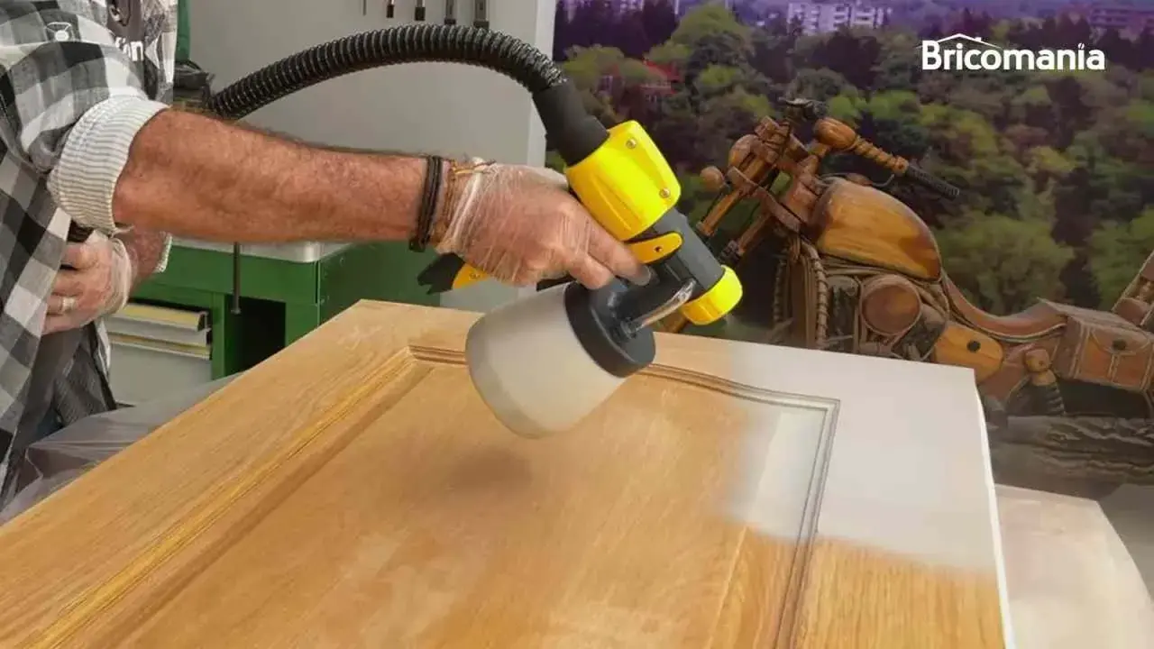 Hombre pintando una puerta de madera con una pistola pulverizadora. El resultado es un acabado liso y uniforme.