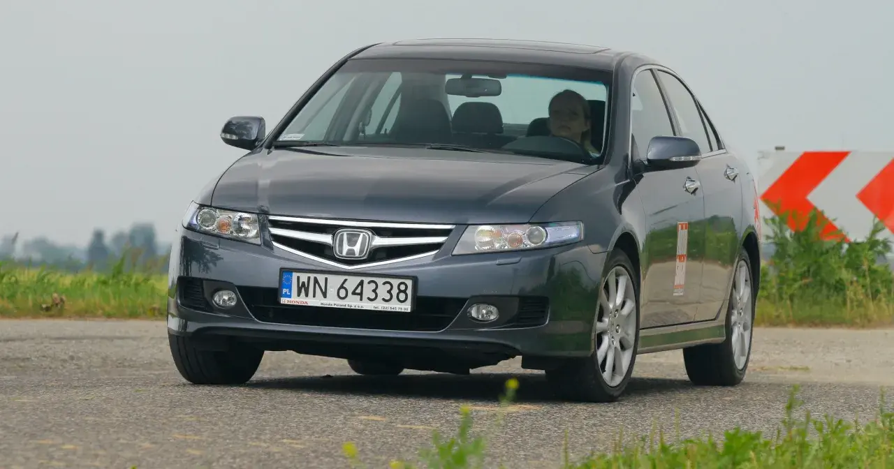 Ciemnoszary Honda Accord z kobietą za kierownicą jedzie po drodze.