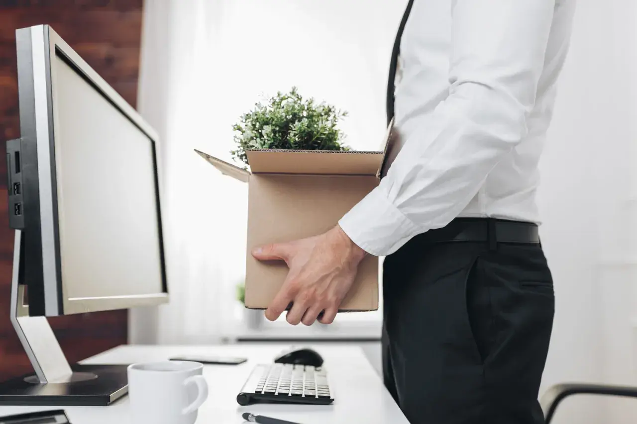 Un employé quitte son bureau, emportant ses affaires dans un carton. Il s'apprête à recevoir son solde tout compte imposable.