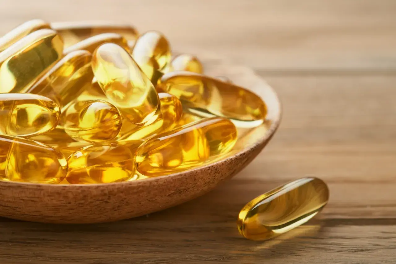 Goldene Kapseln auf einem Holzlöffel, die die positive Wirkung von Omega-3 auf die Psyche symbolisieren.