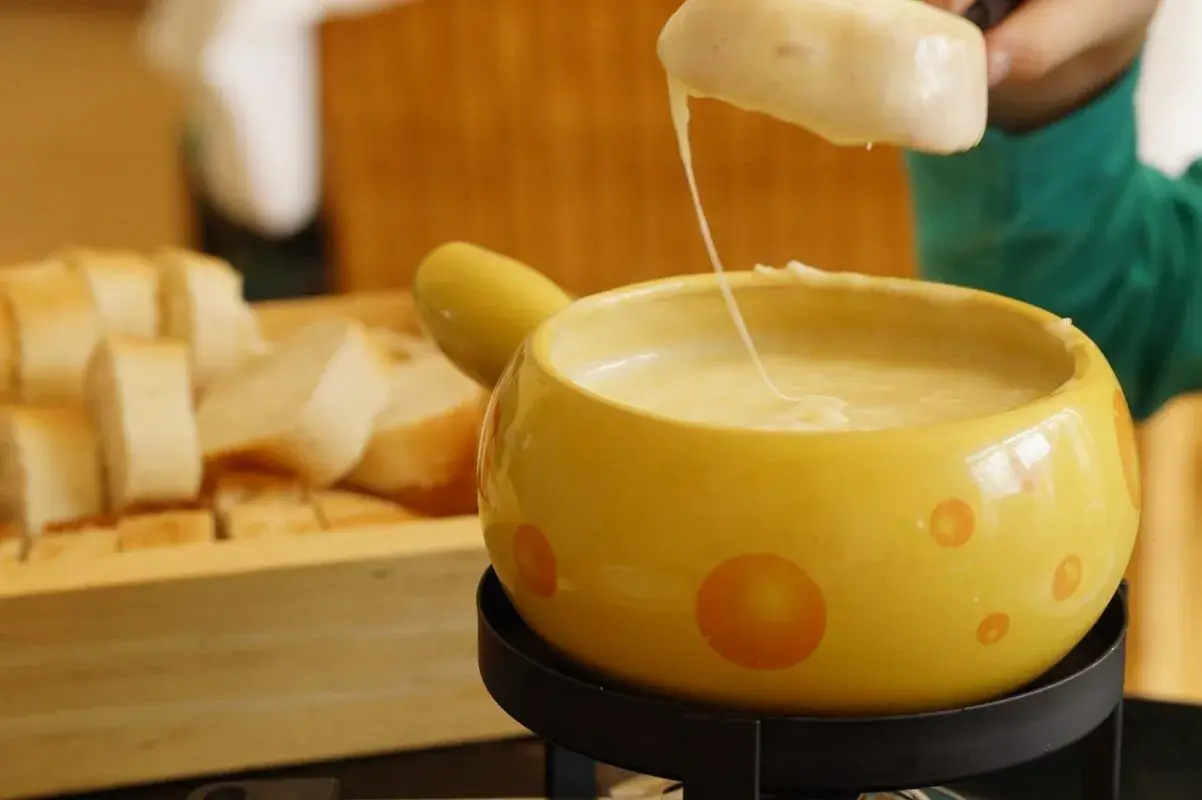 Un pezzo di pane viene intinto in una fonduta di pecorino fumante, servita in una ciotola gialla decorata.