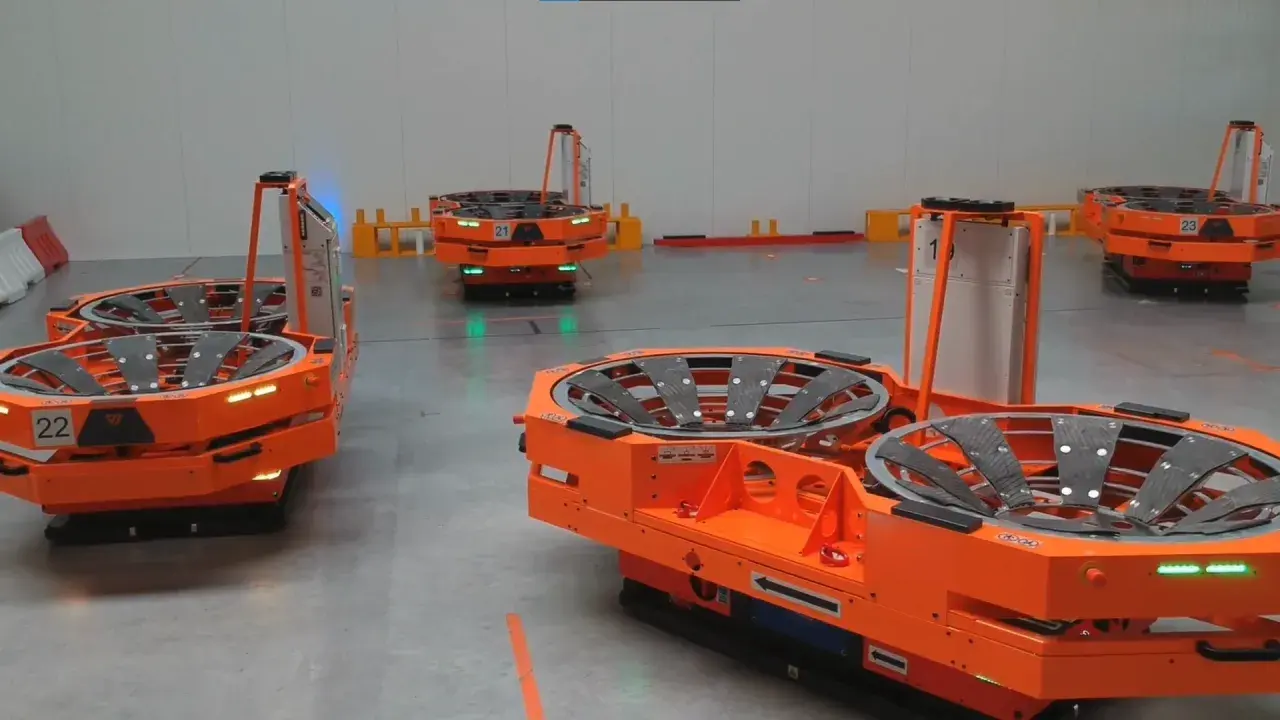 Pomarańczowy robot mobilny z numerem 22 w magazynie. W tle inne roboty i regały.