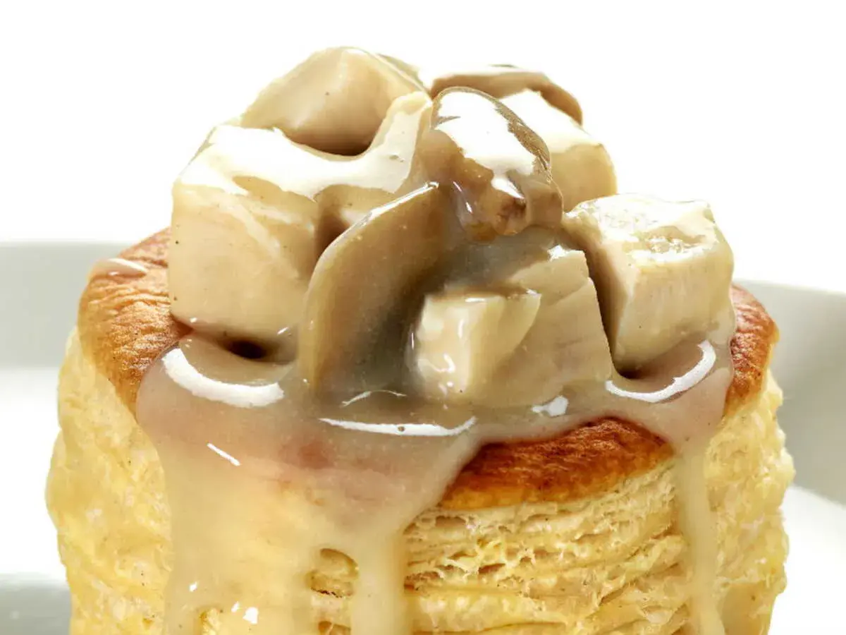 Une bouchée à la reine poulet, garnie de morceaux de volaille et d'une sauce crémeuse aux champignons, sur une pâte feuilletée dorée.