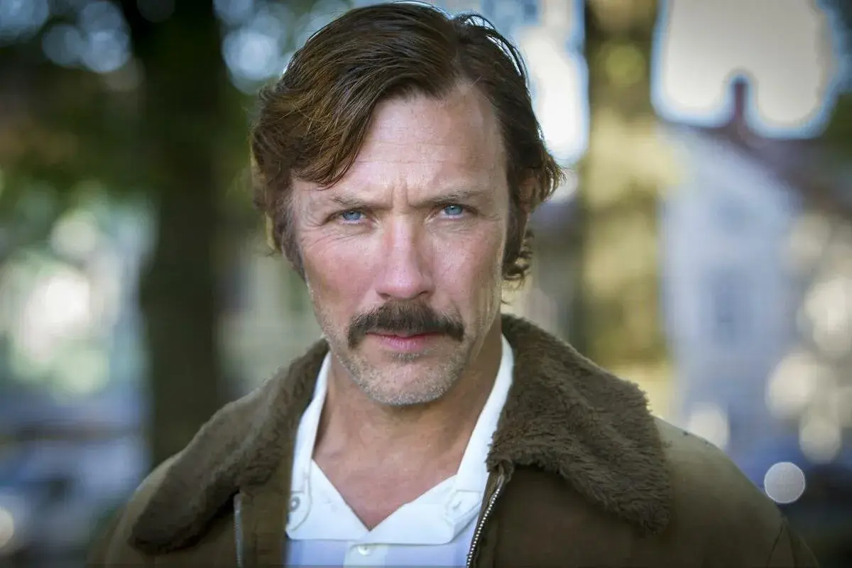 Porträtt av en svensk manlig skådespelare från Dramaten med mustasch och blå ögon, klädd i en brun jacka med foder.