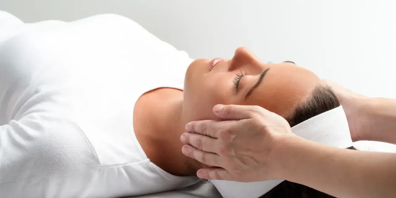 Kobieta w białej koszulce doświadcza relaksującego dotyku dłoni. To może być właśnie reiki co to za technika, która przynosi ukojenie.