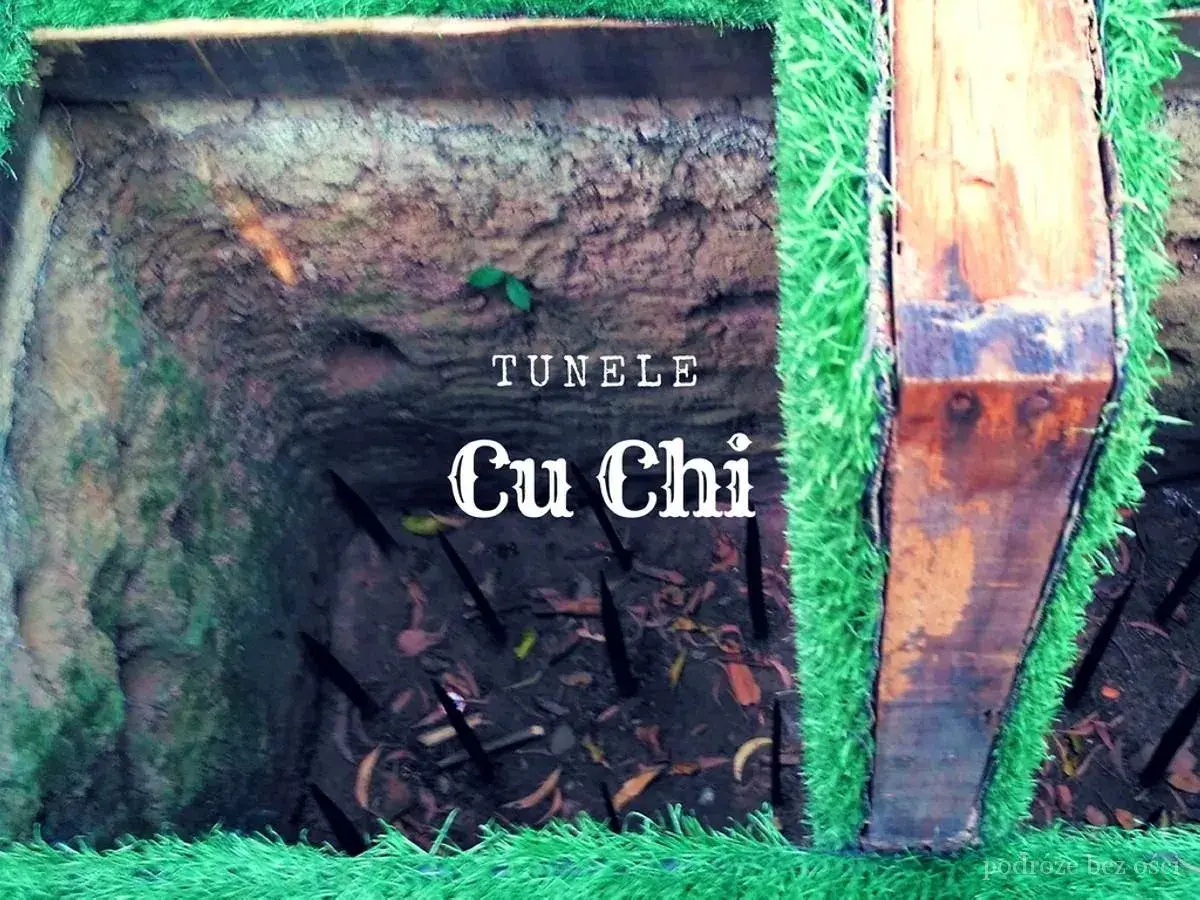 Wejście do tuneli Cu Chi, z ostrymi zaostrzonymi palami w dole. Sztuczna trawa otacza drewniane wsparcie.
